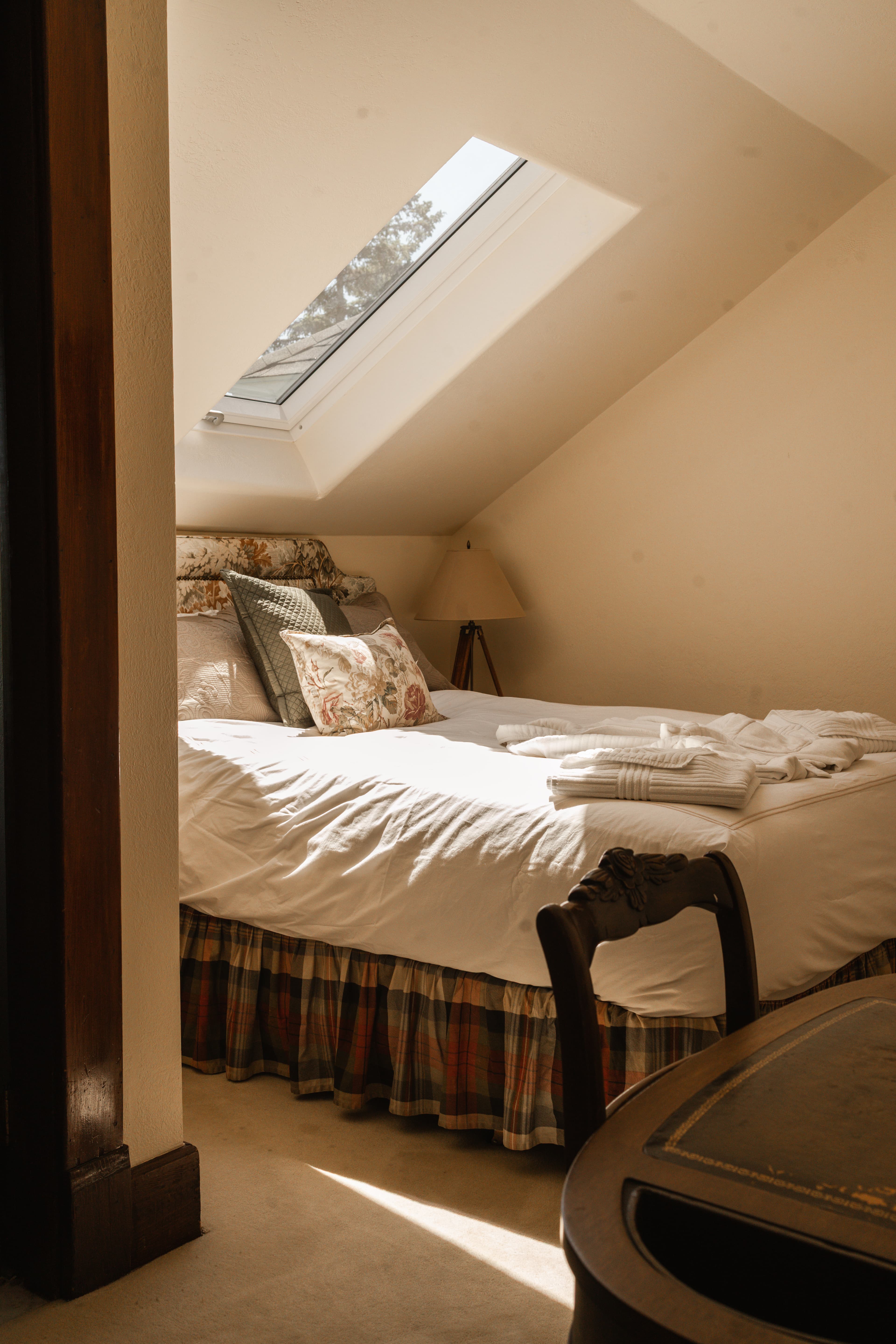 Cozy bedroom with a slanted skylight, neatly made bed, and a lamp.