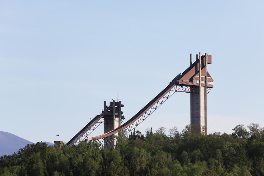 Ski jump ramp rising above green trees under a clear blue sky.