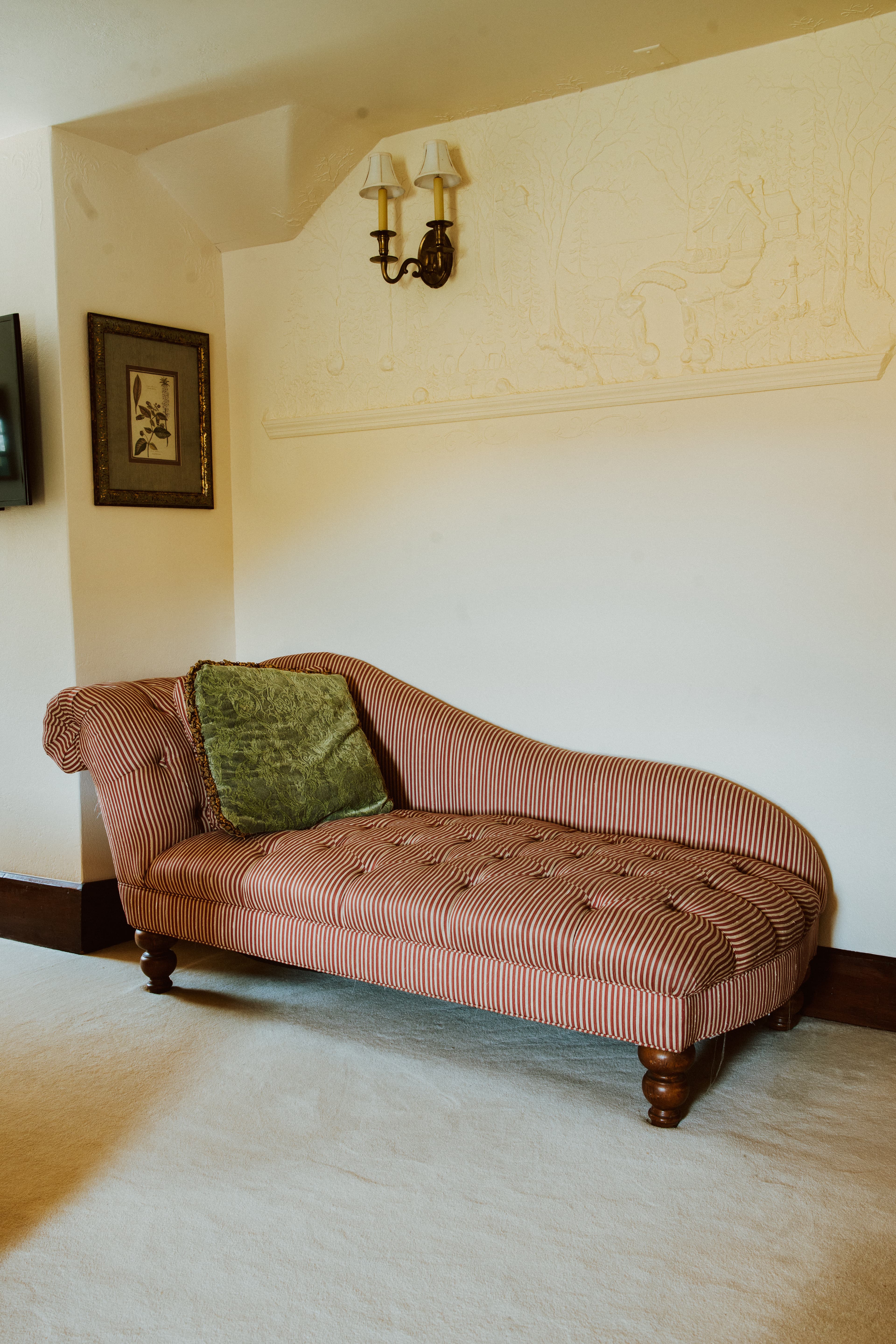 A striped chaise lounge with a green cushion against a white wall.