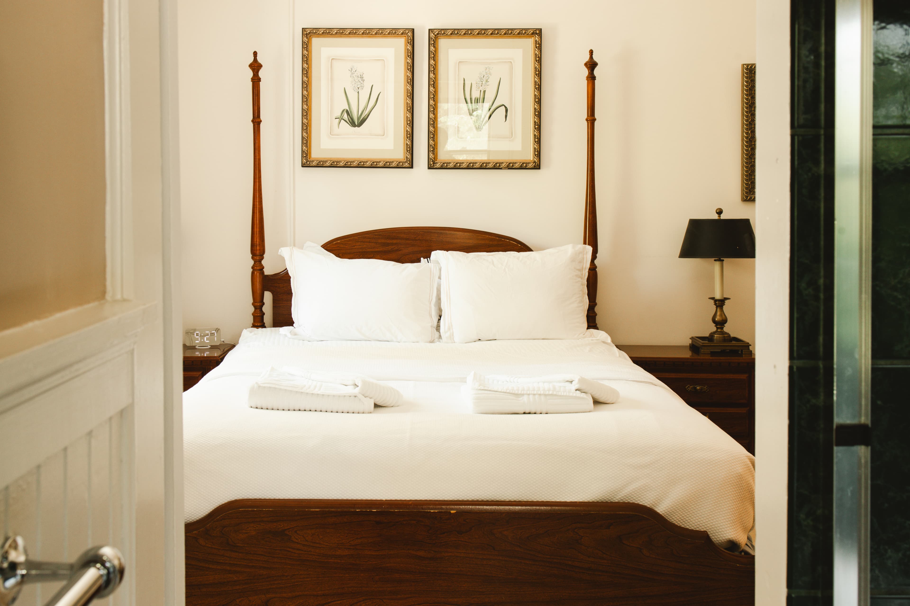 A well-decorated bedroom with a wooden bed, white linens, and framed botanical art on the walls.