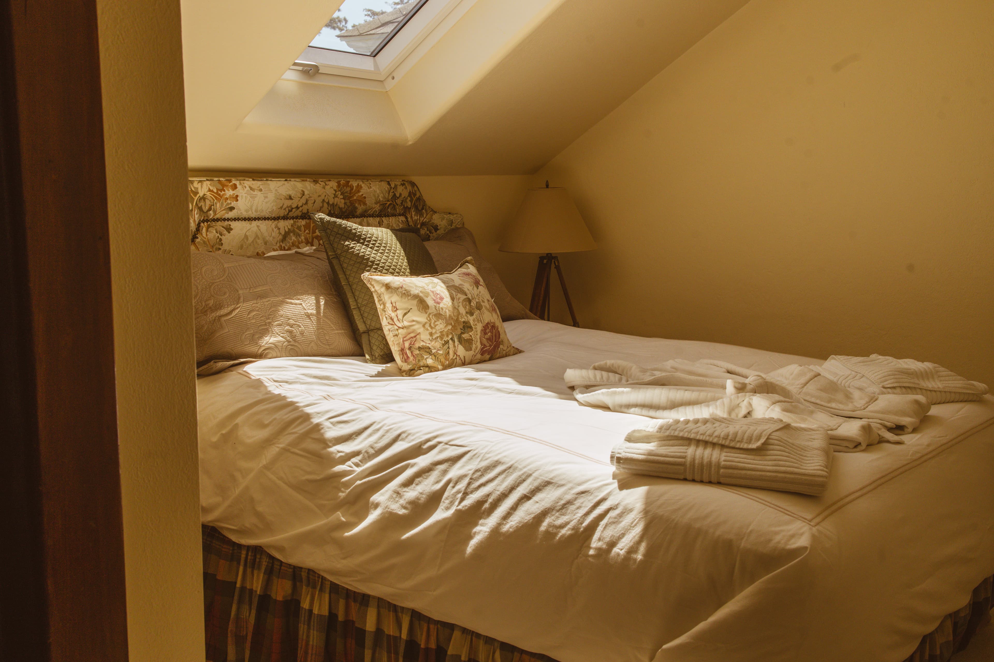 Cozy bedroom with a neatly made bed, decorative pillows, and a skylight.