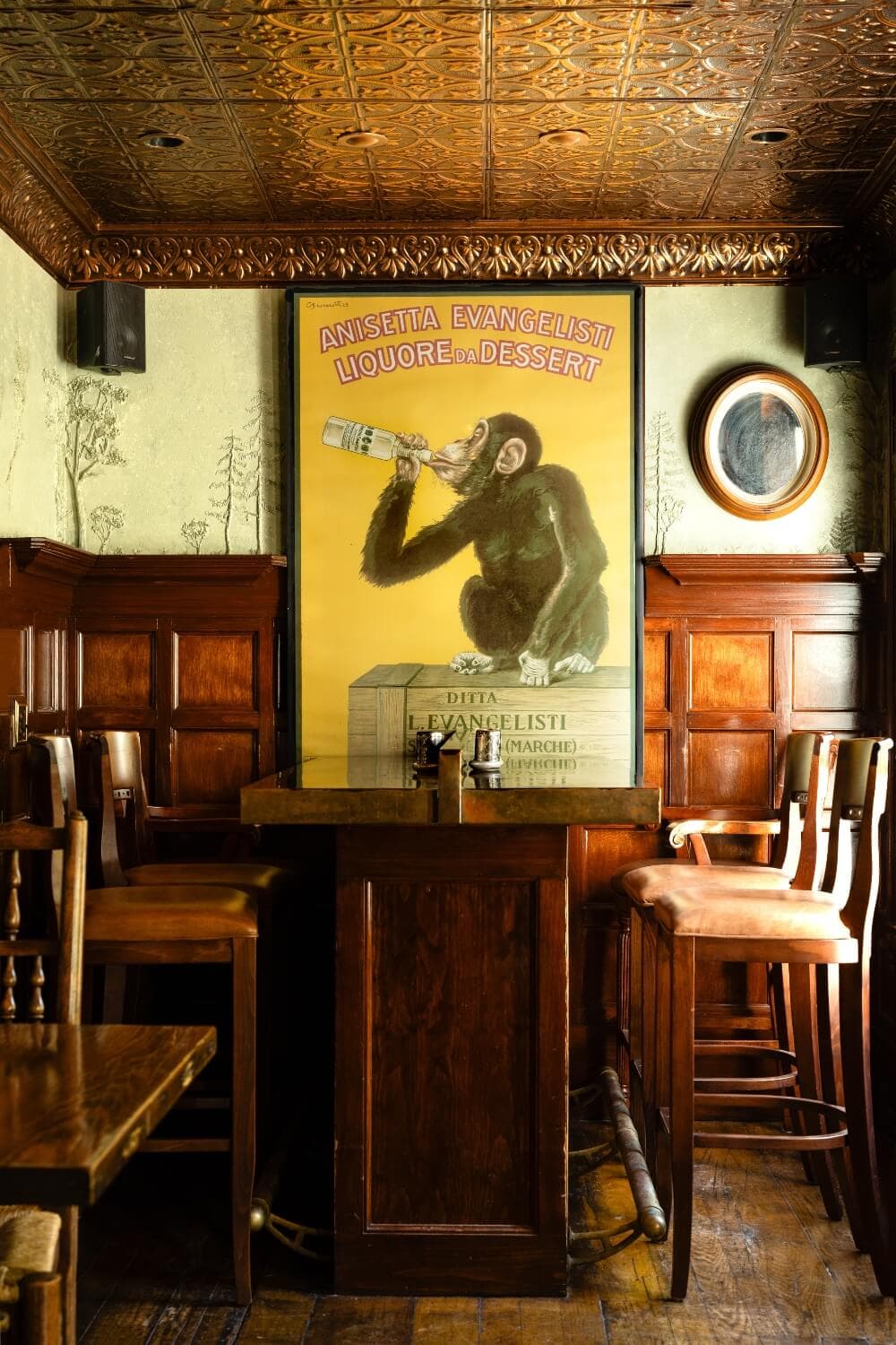 A cozy bar interior featuring wooden furniture and a vintage advertisement of a monkey drinking liquor.