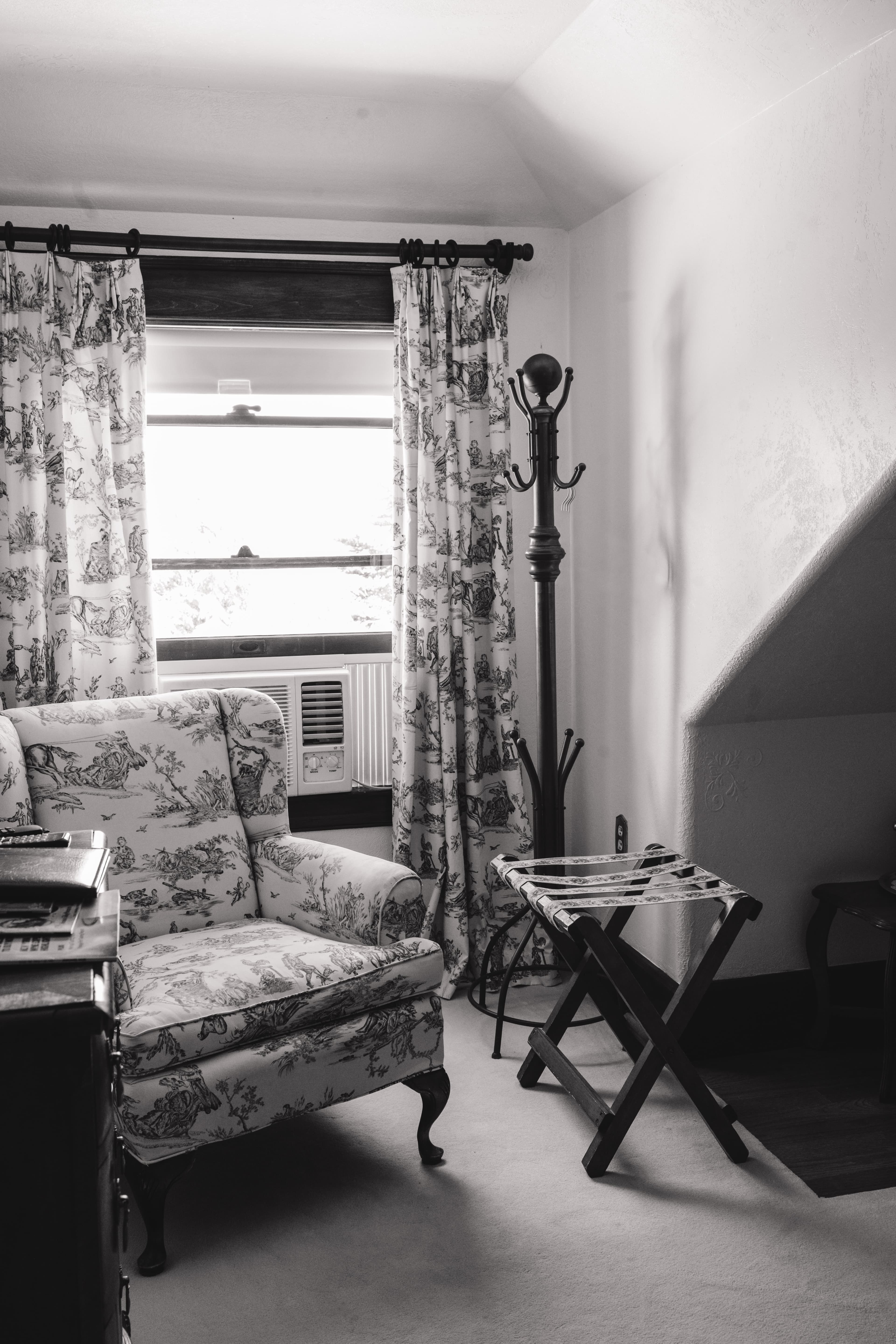 Cozy corner with a patterned armchair, window with curtains, and a small folding table.