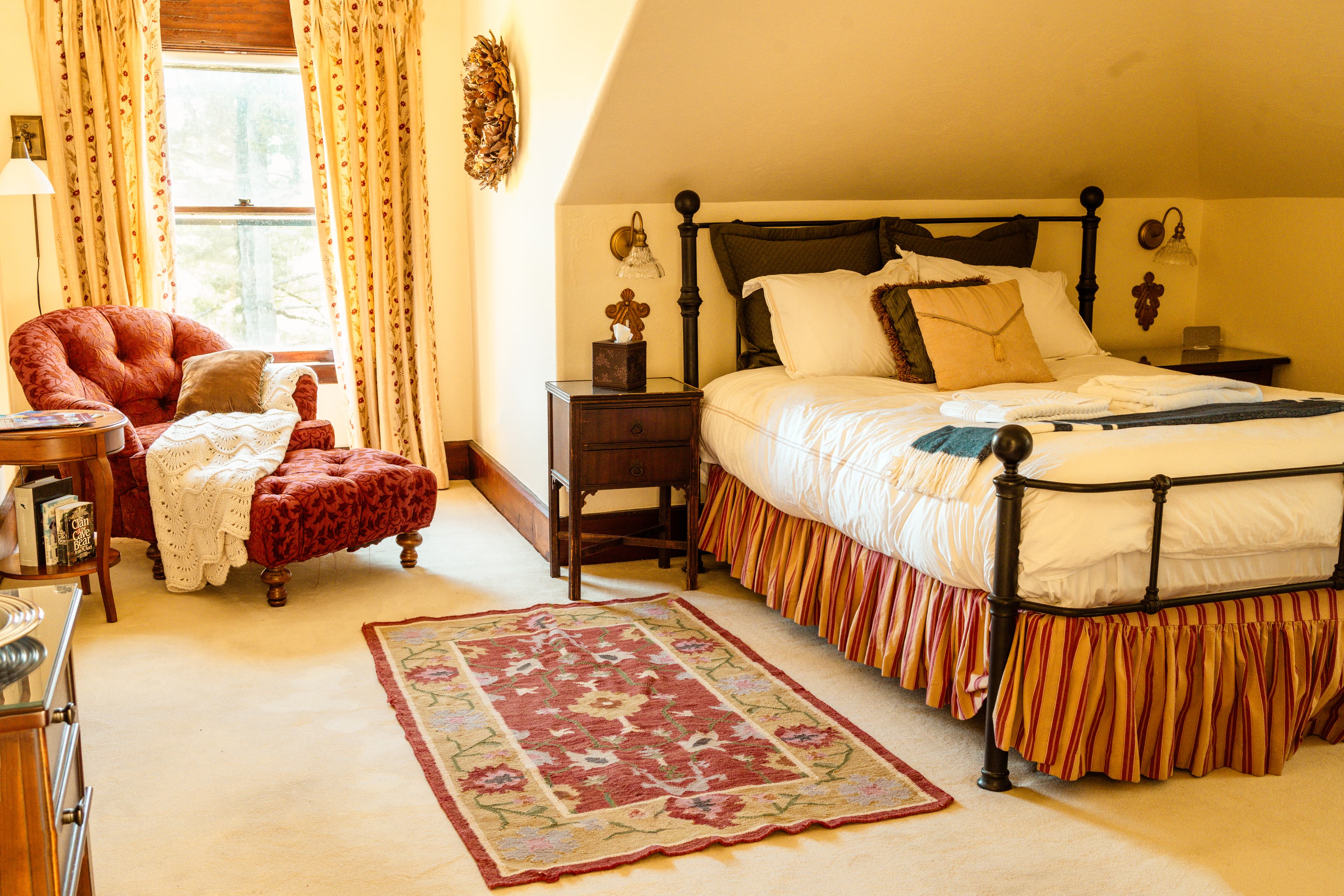 A cozy bedroom featuring a vintage bed, plush chair, and decorative rug.