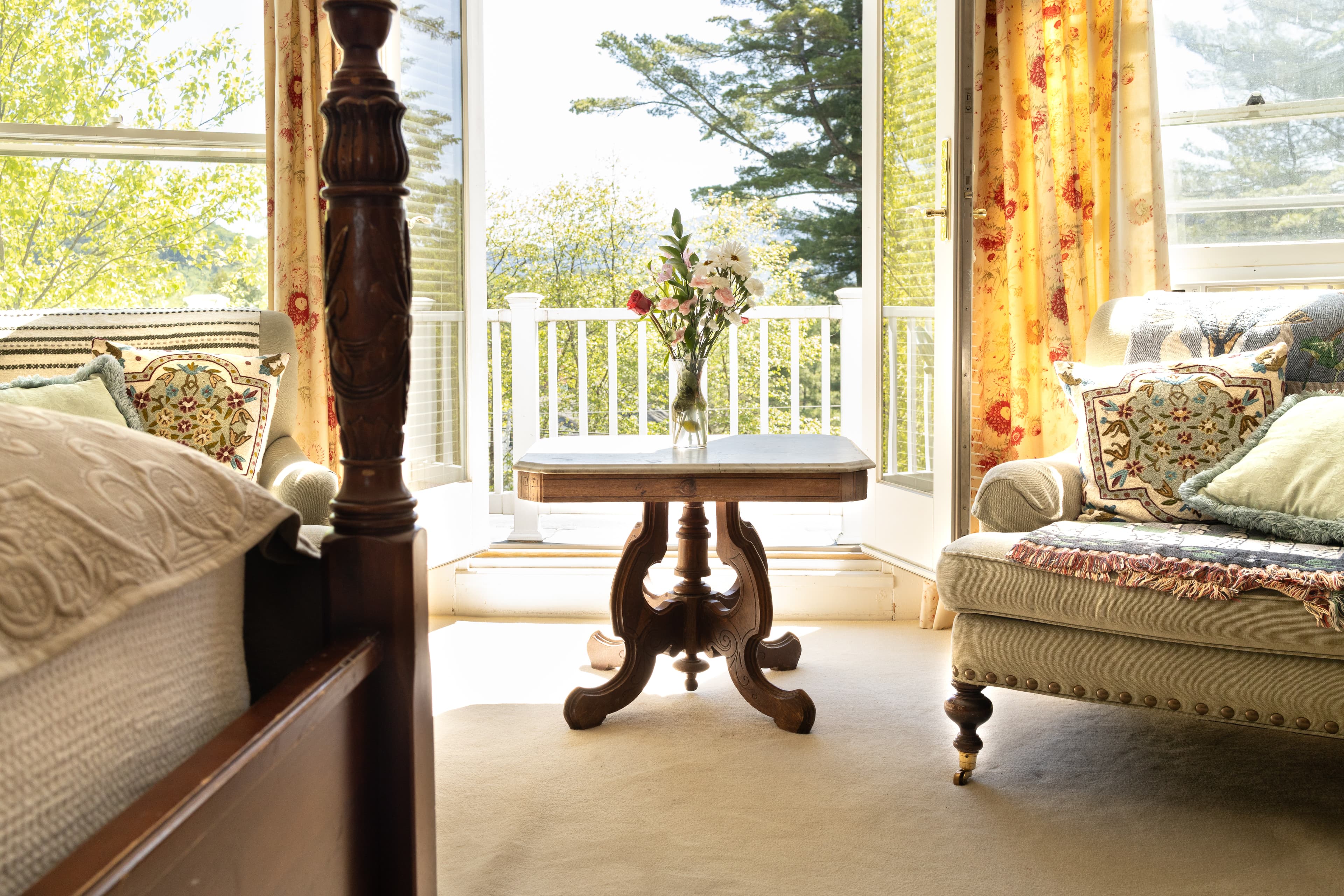 A cozy room with sunlight streaming in, featuring a wooden table and comfortable seating near an open balcony.