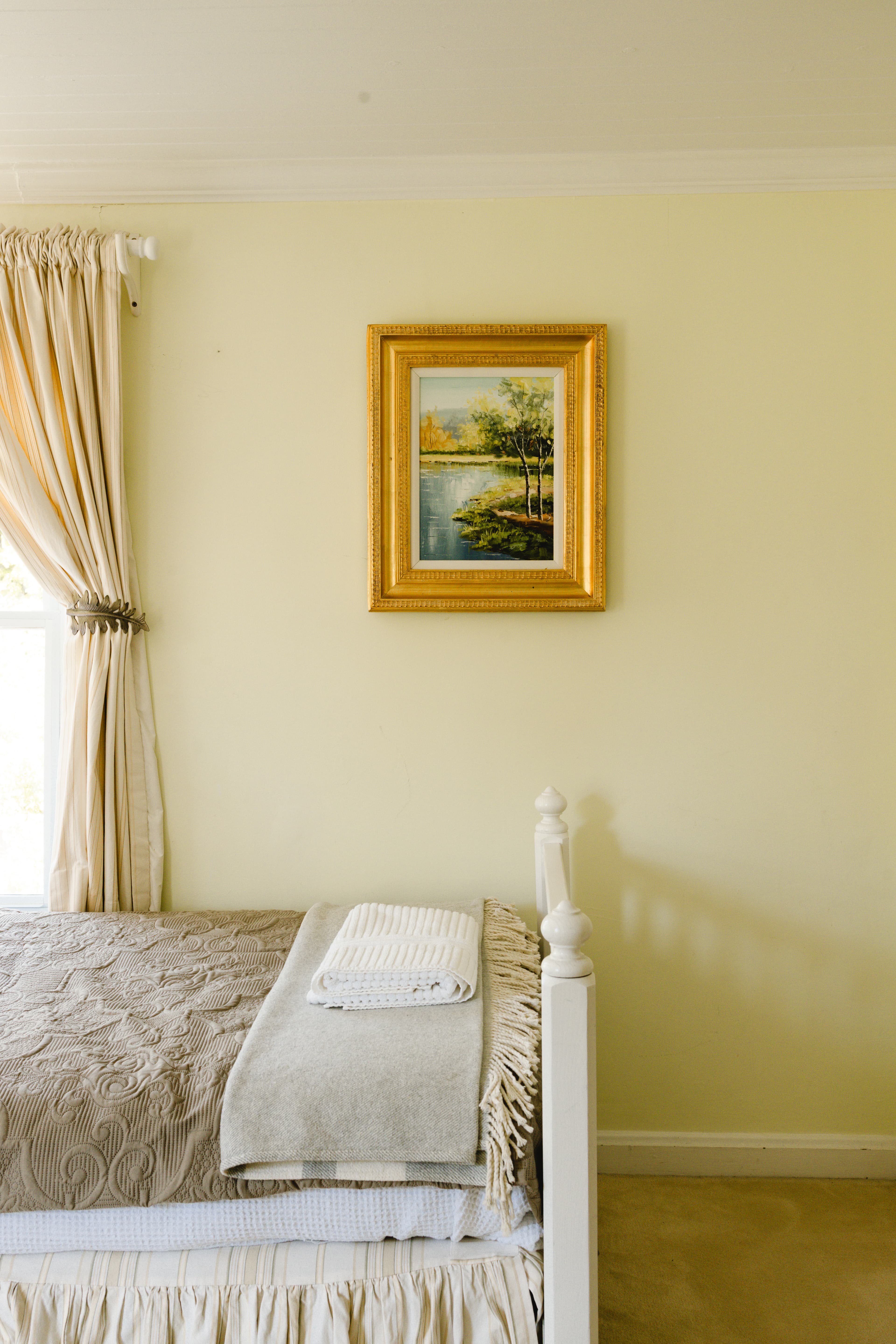 A cozy bedroom featuring a neatly made bed, a small stack of towels, and a framed painting on the wall.