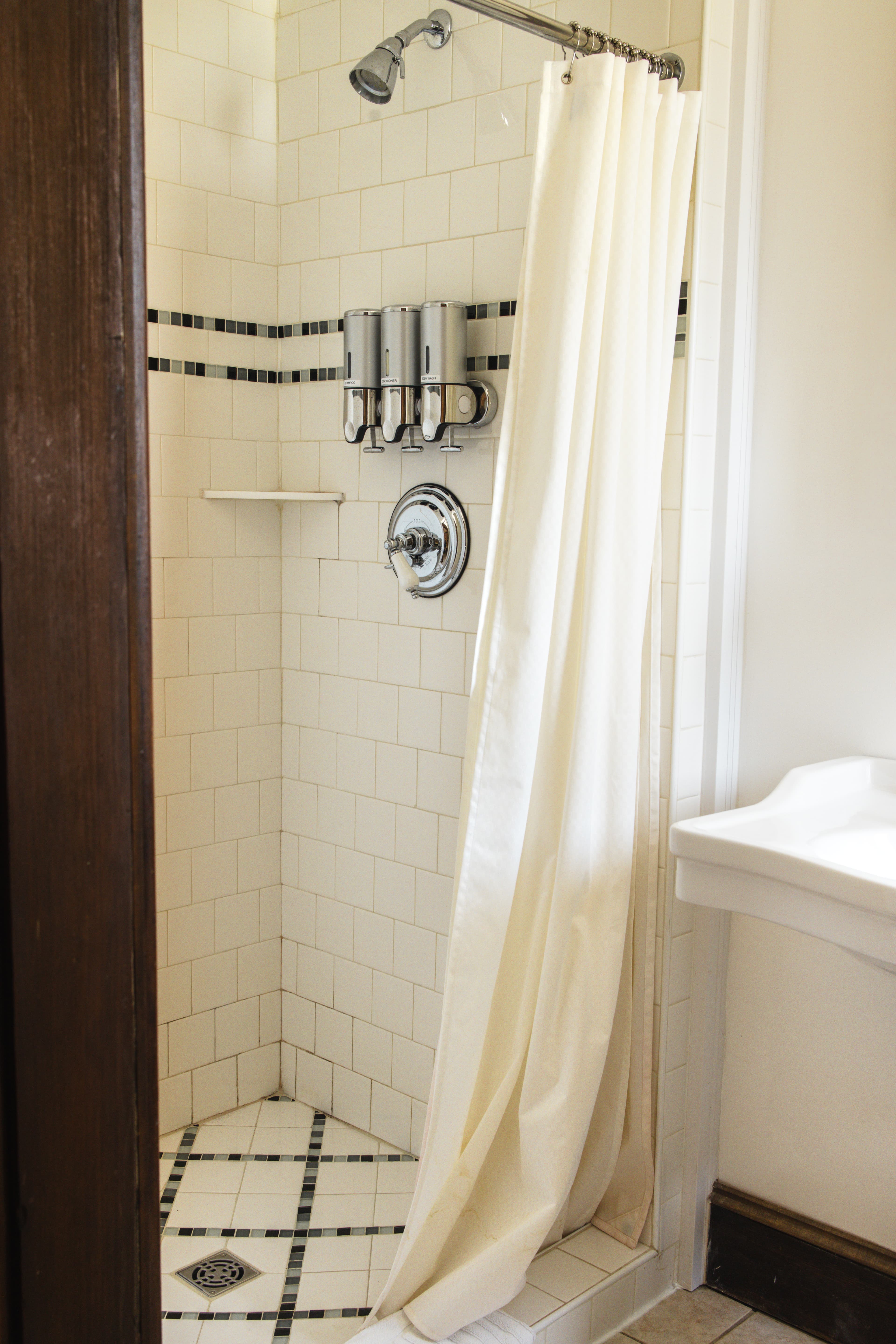 Shower area featuring a white curtain, tiled walls, and wall-mounted shampoo dispensers.