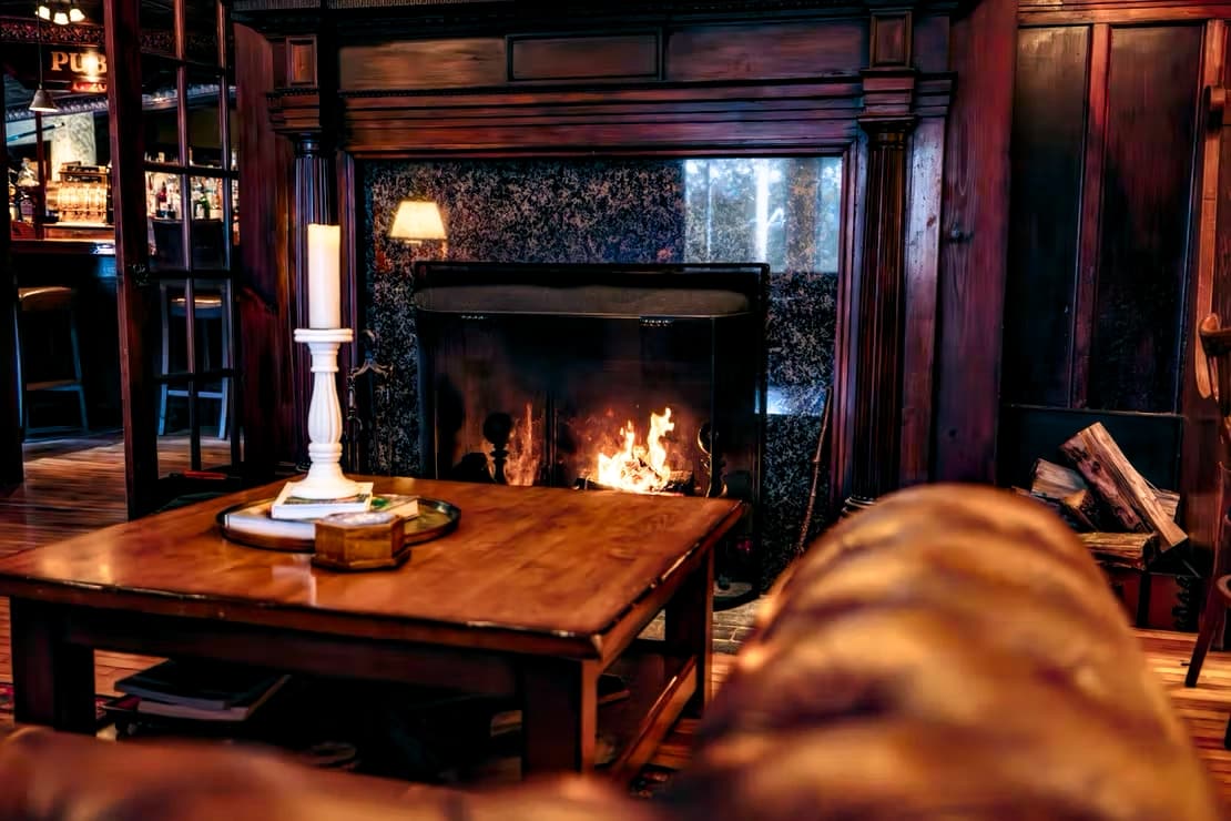 A cozy living room featuring a flickering fireplace, a wooden table with a candle, and leather seating.