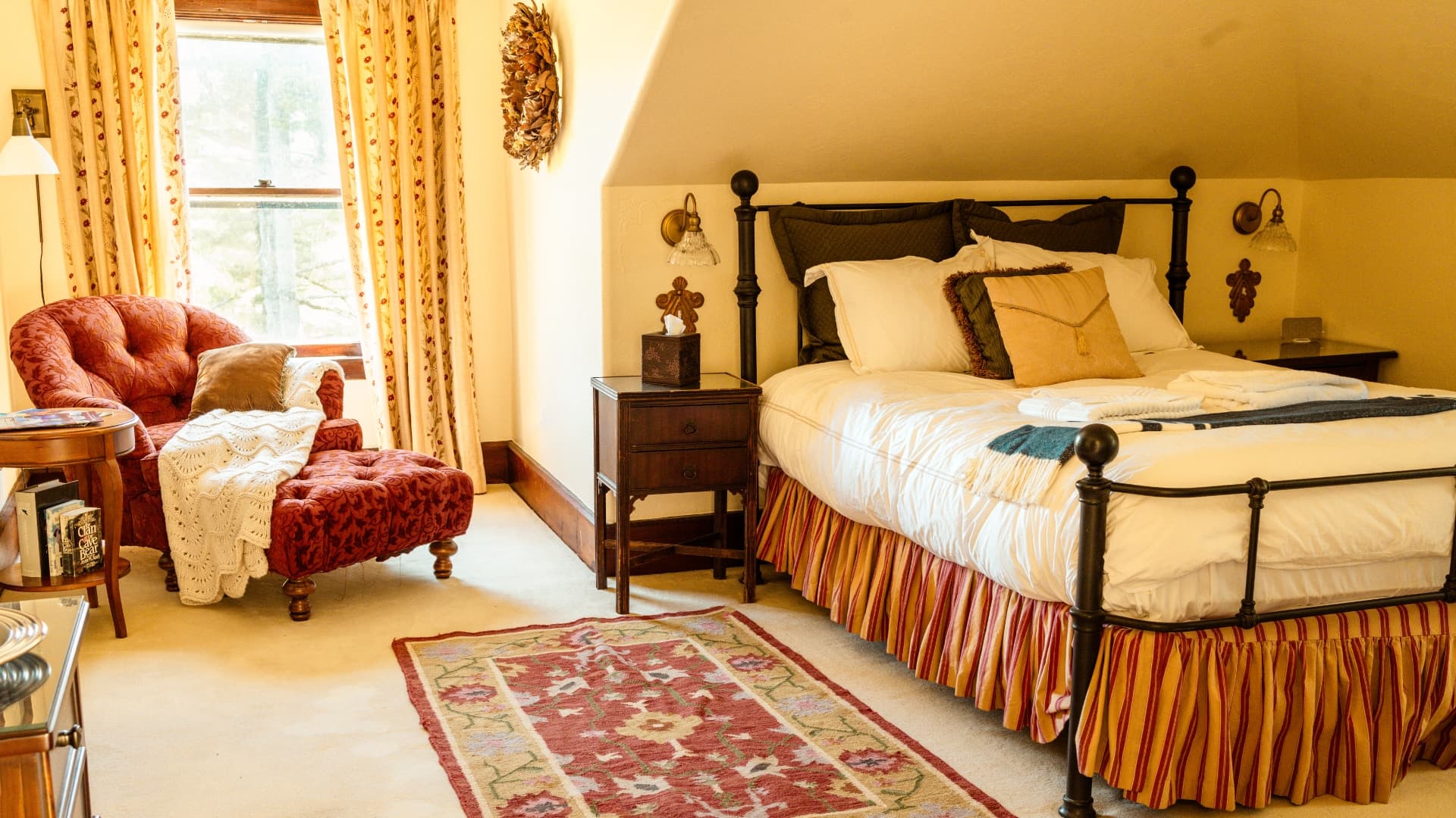 A cozy bedroom featuring a metal bed, red armchair, and floral rug.