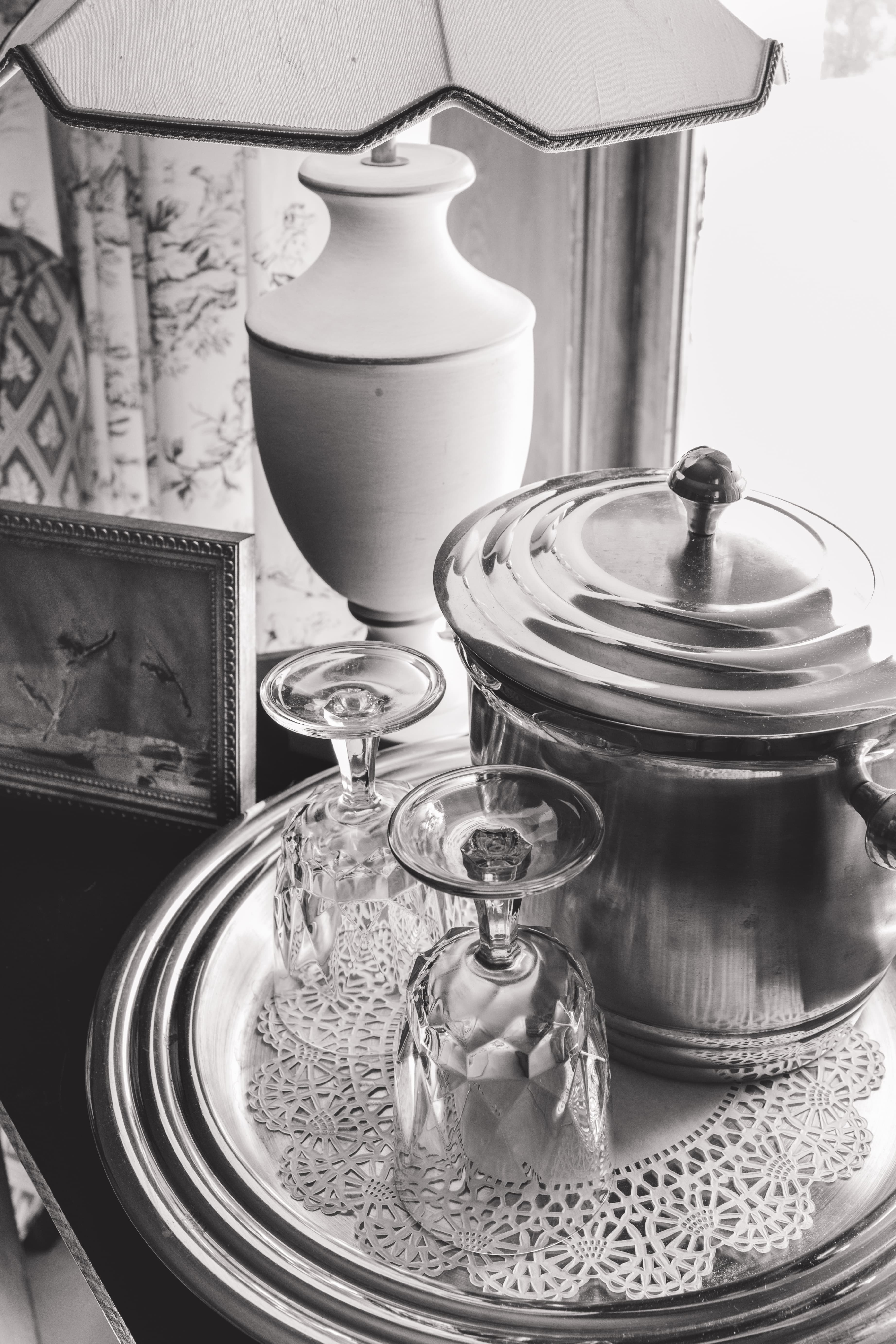 A vintage setting featuring a lamp, a decorative frame, an ice bucket, and two crystal glasses on a silver tray.