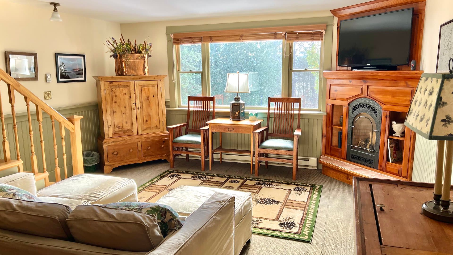 Cozy living room featuring a sofa, wooden furniture, and a fireplace with natural light from large windows.