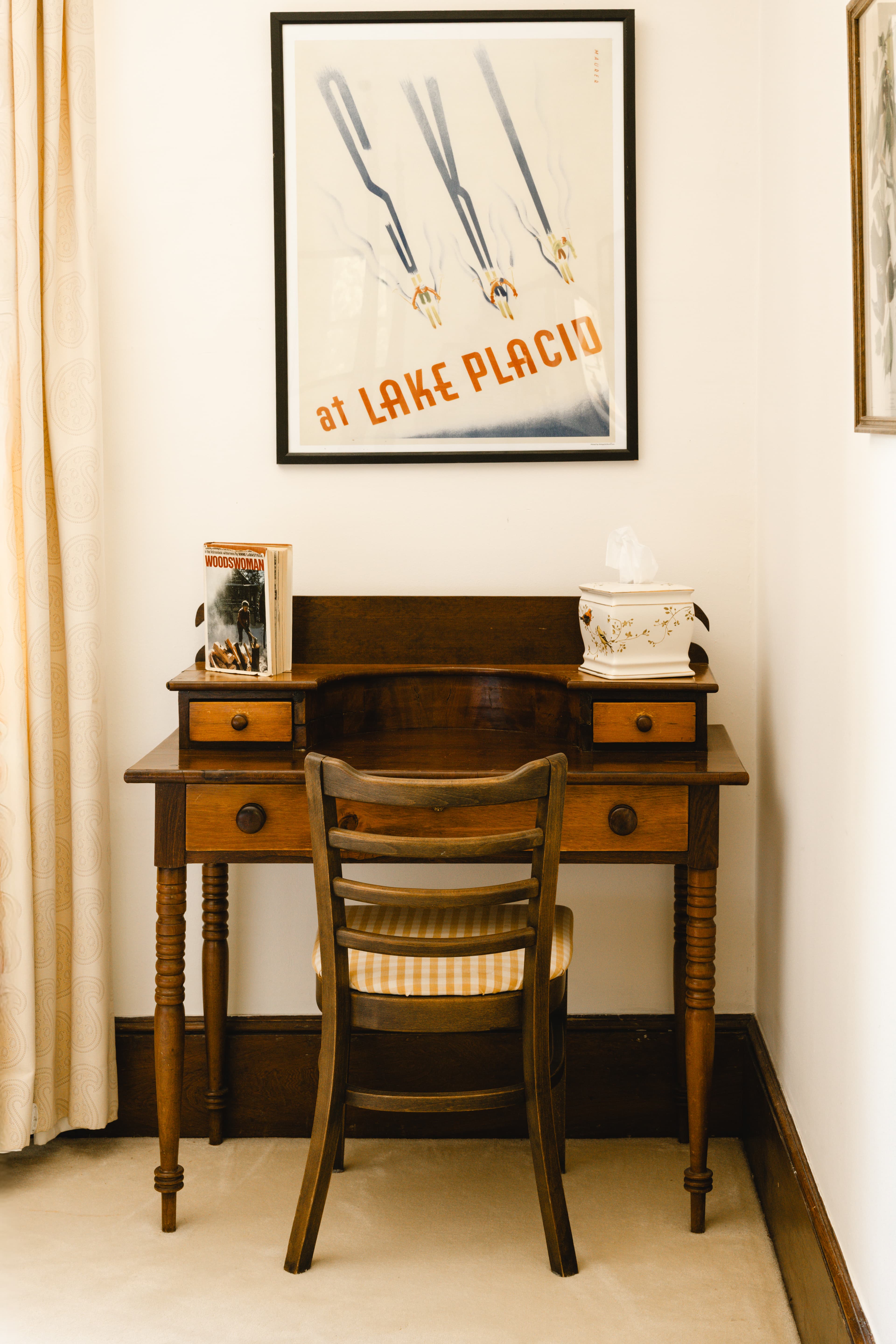 A vintage wooden desk with a chair beneath a skiing poster and books.
