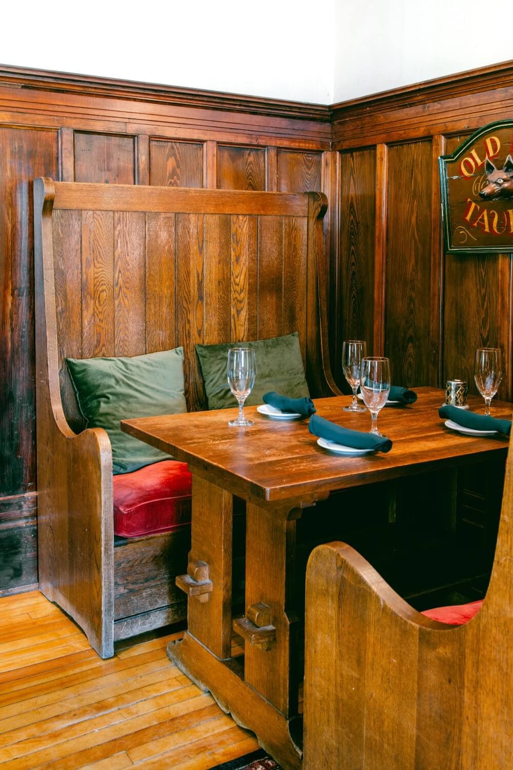 A wooden dining booth with green pillows and a table set for two, against a richly paneled wall.