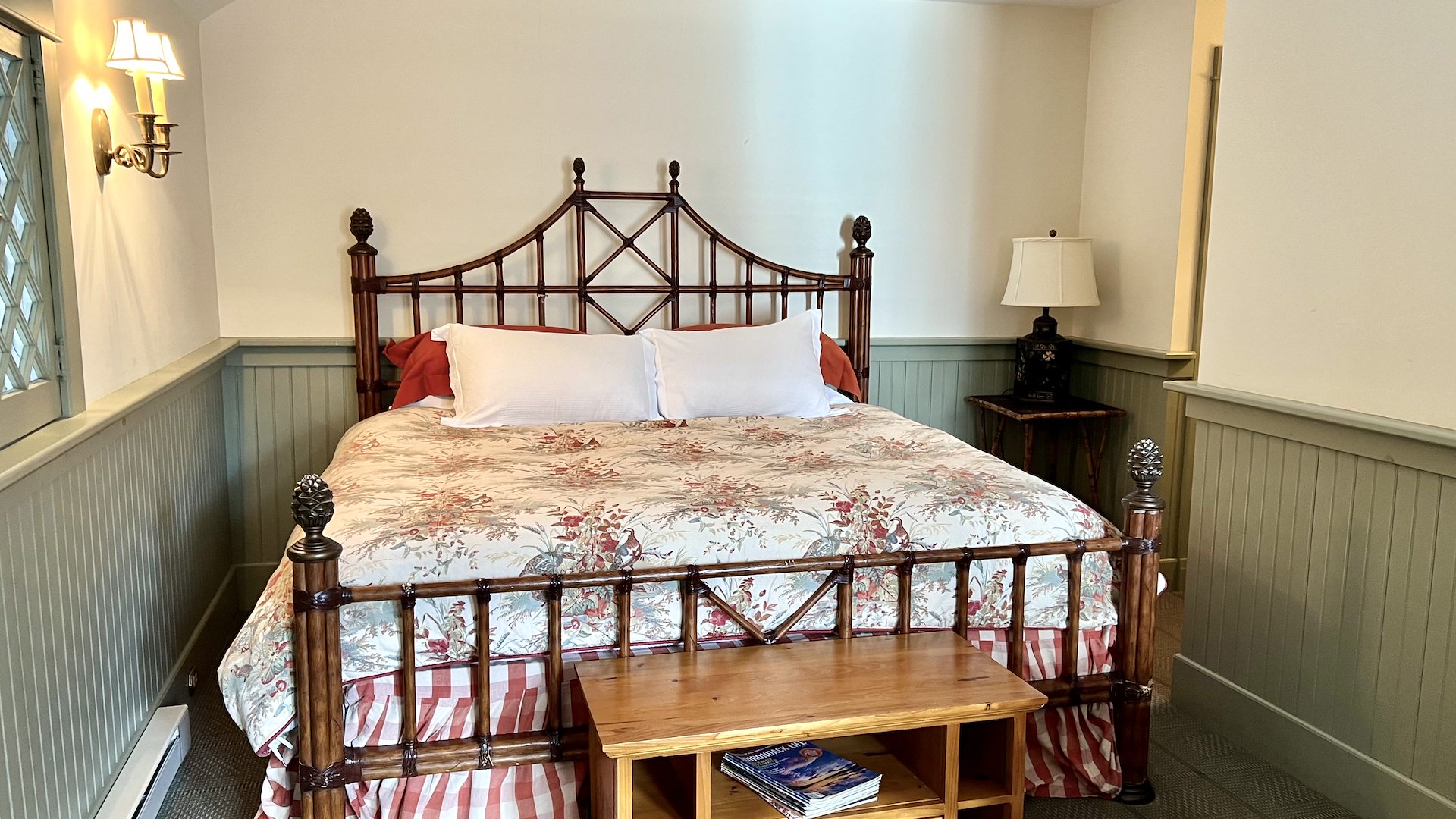 A cozy bedroom featuring a floral-patterned bed, a wooden bedside table, and warm lighting.