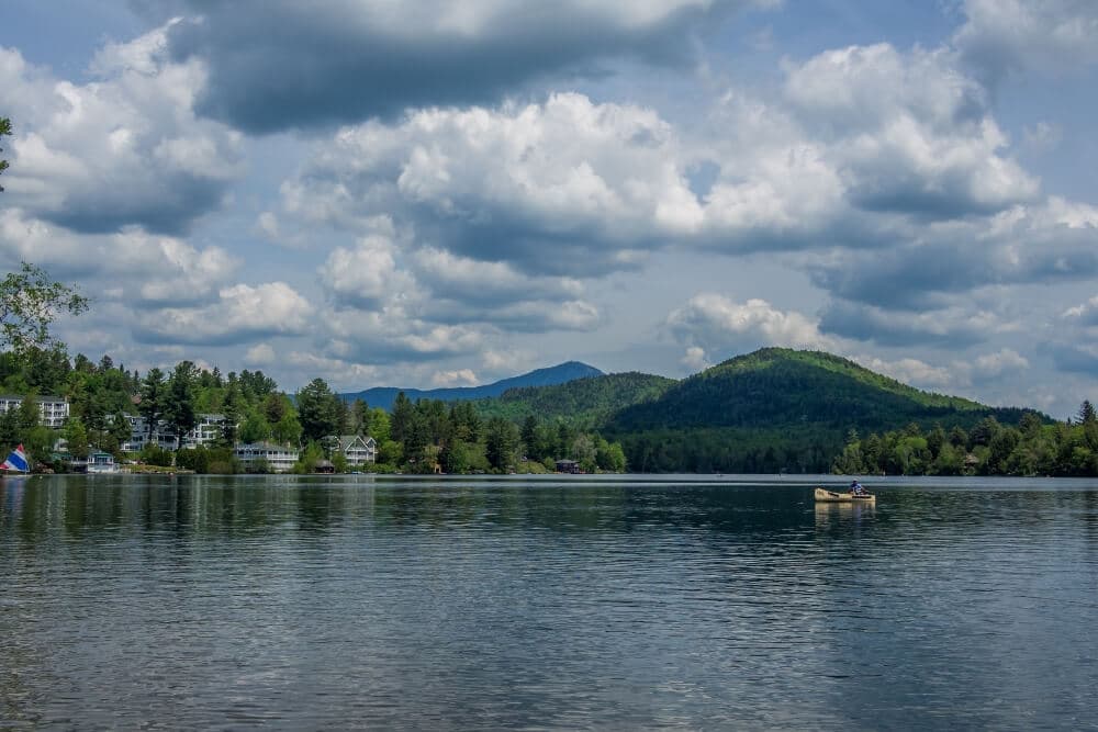 A serene lake surrounded by green mountains and dotted with fluffy clouds.