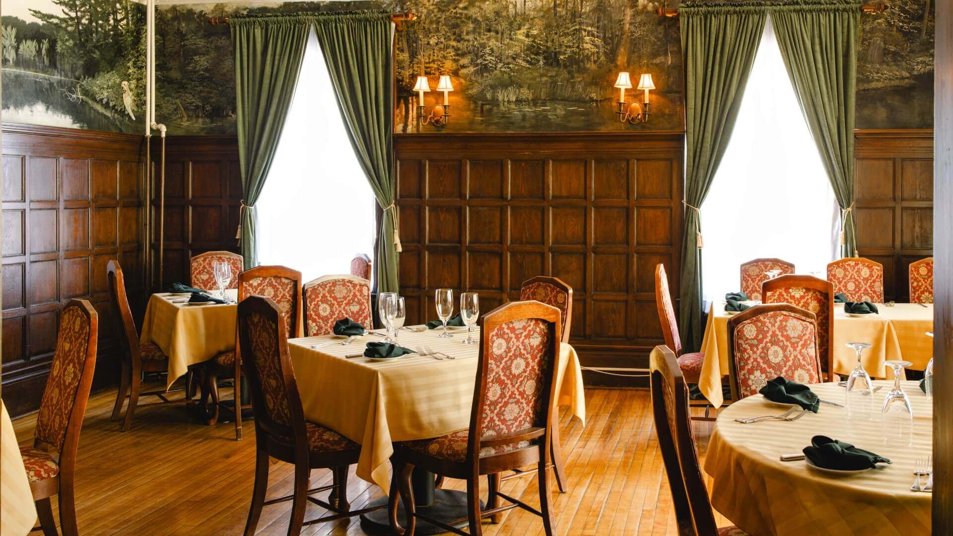 A dimly lit, elegantly furnished restaurant with wooden walls and tables set for dining.