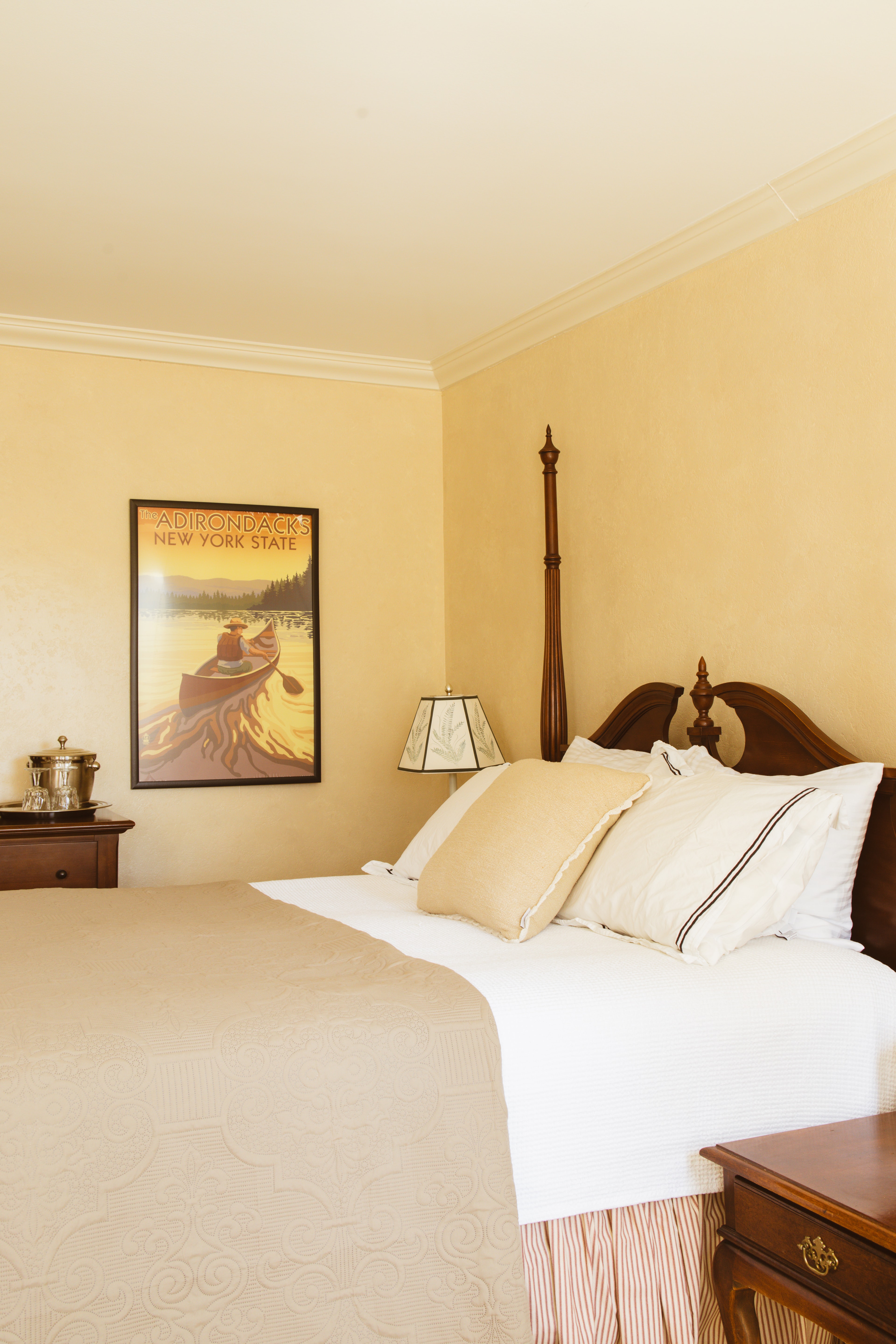 A cozy bedroom featuring a vintage Adirondack poster, a wooden bed with decorative pillows, and bedside furnishings.