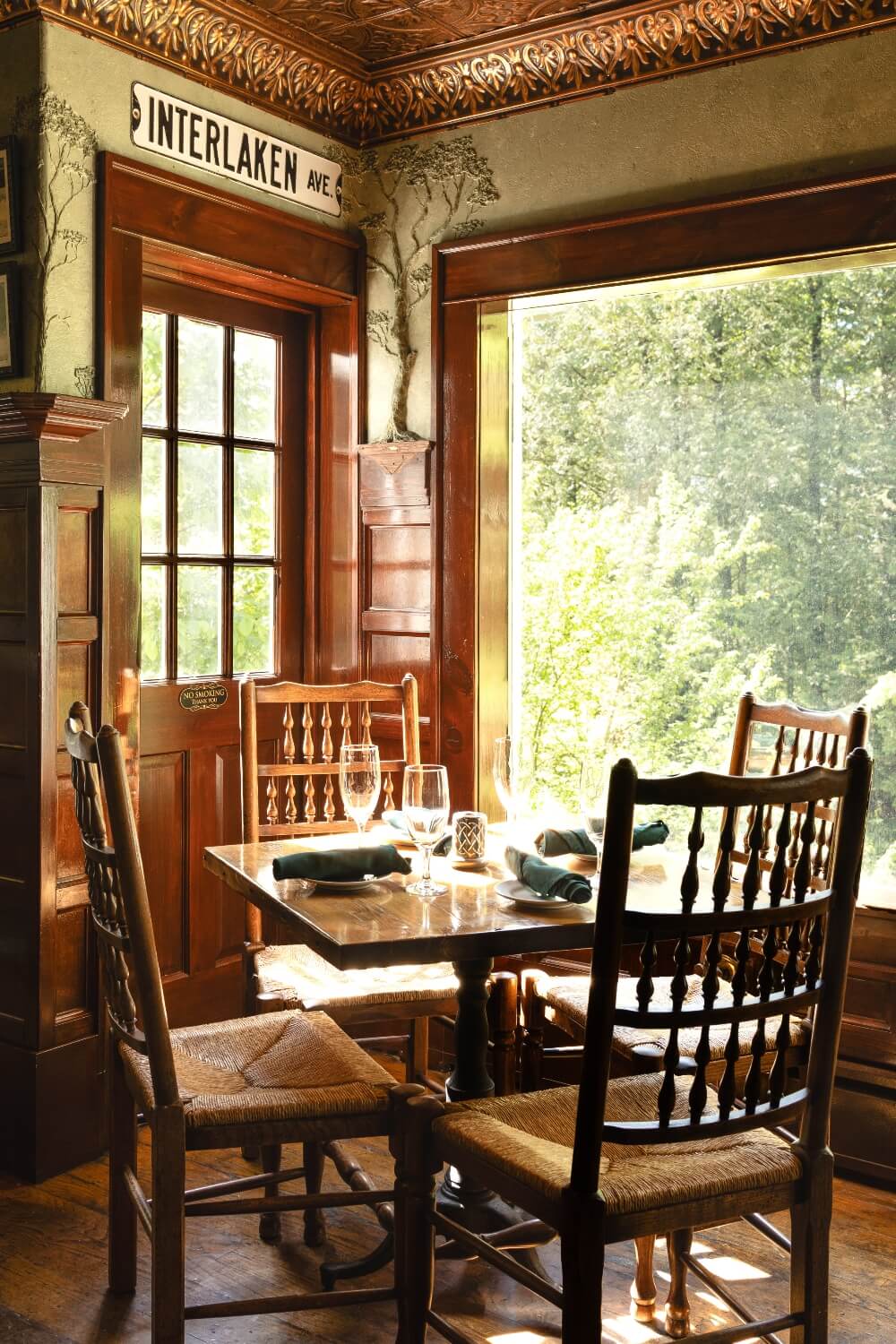 Cozy dining area with wooden furniture and a view of greenery through a large window.
