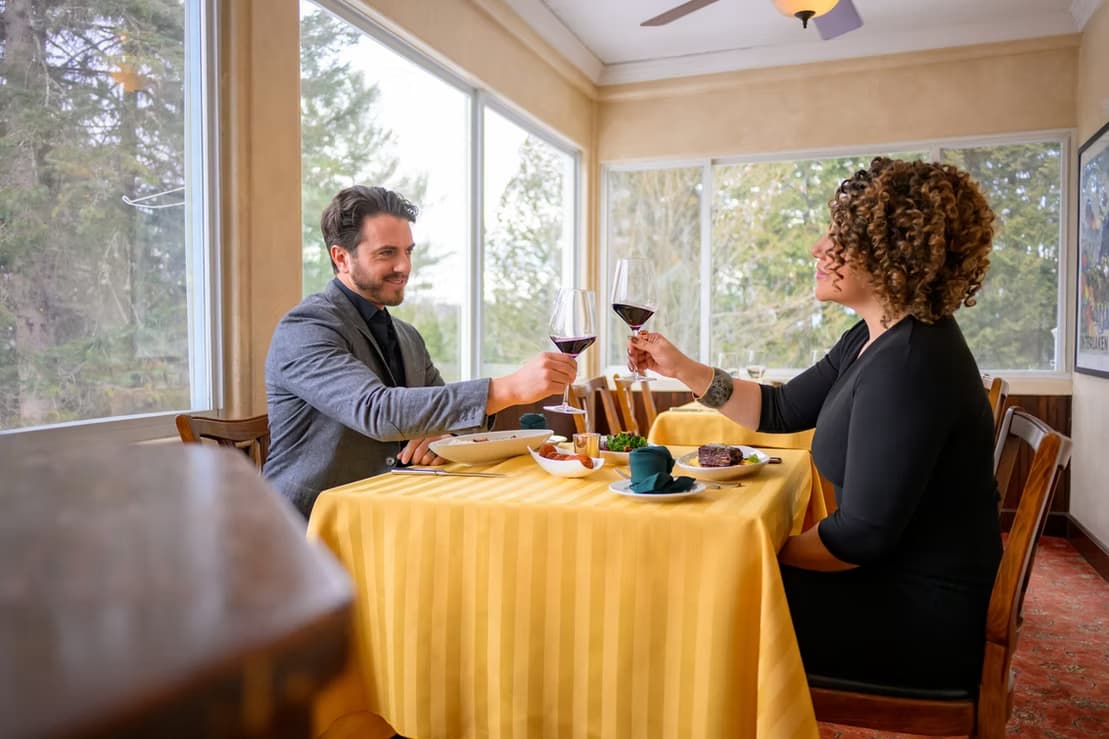 A man and woman toast with glasses of red wine at a cozy table in a restaurant.