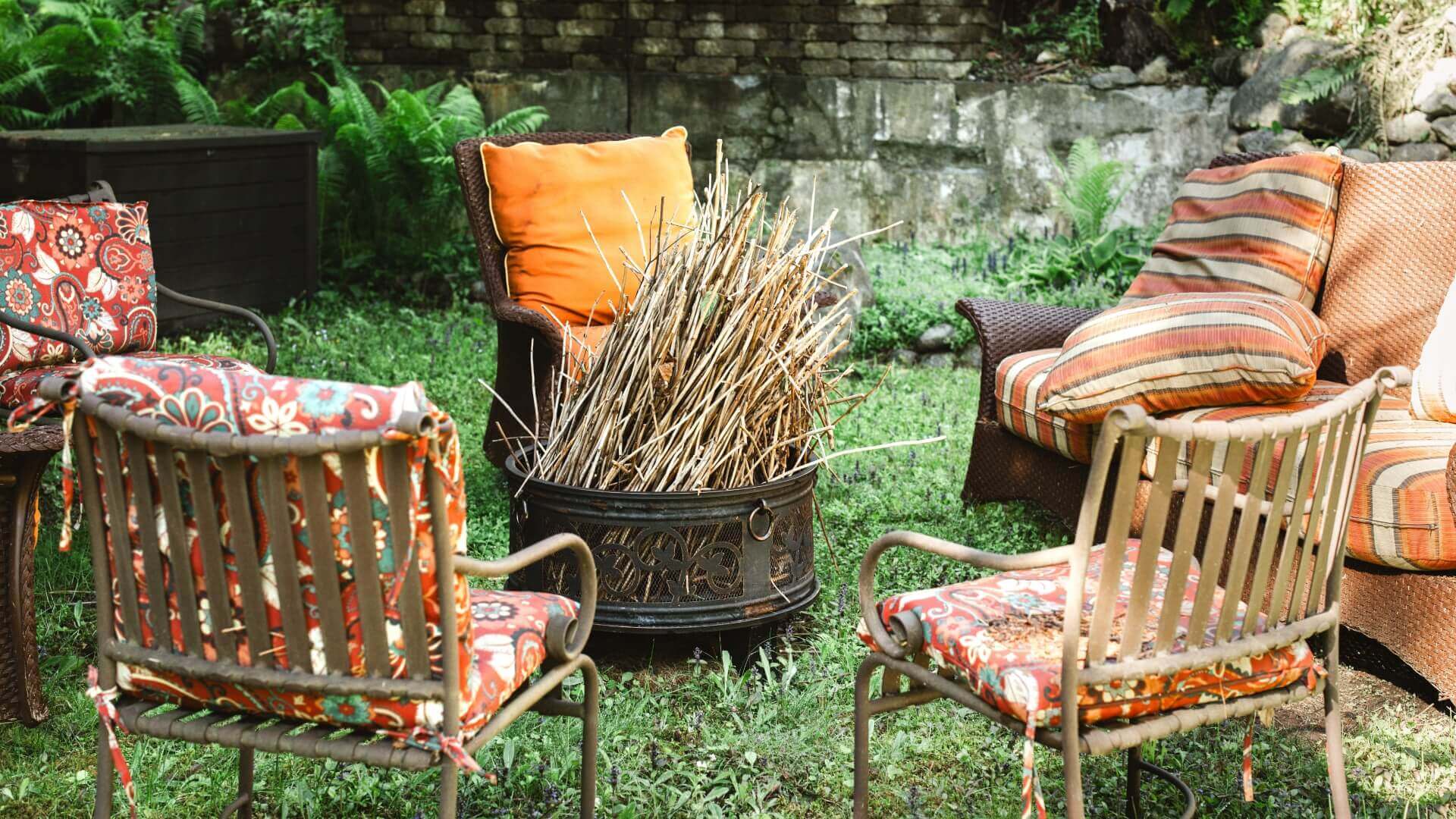 A cozy outdoor seating area with patterned cushions surrounding a fire pit filled with sticks.