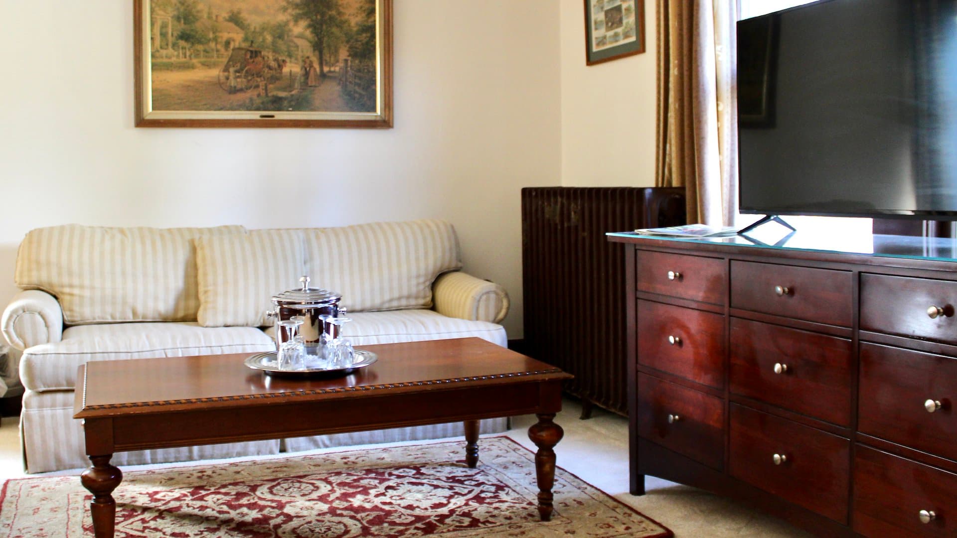 A cozy living room featuring a striped sofa, wooden coffee table, and a television beside a radiator.