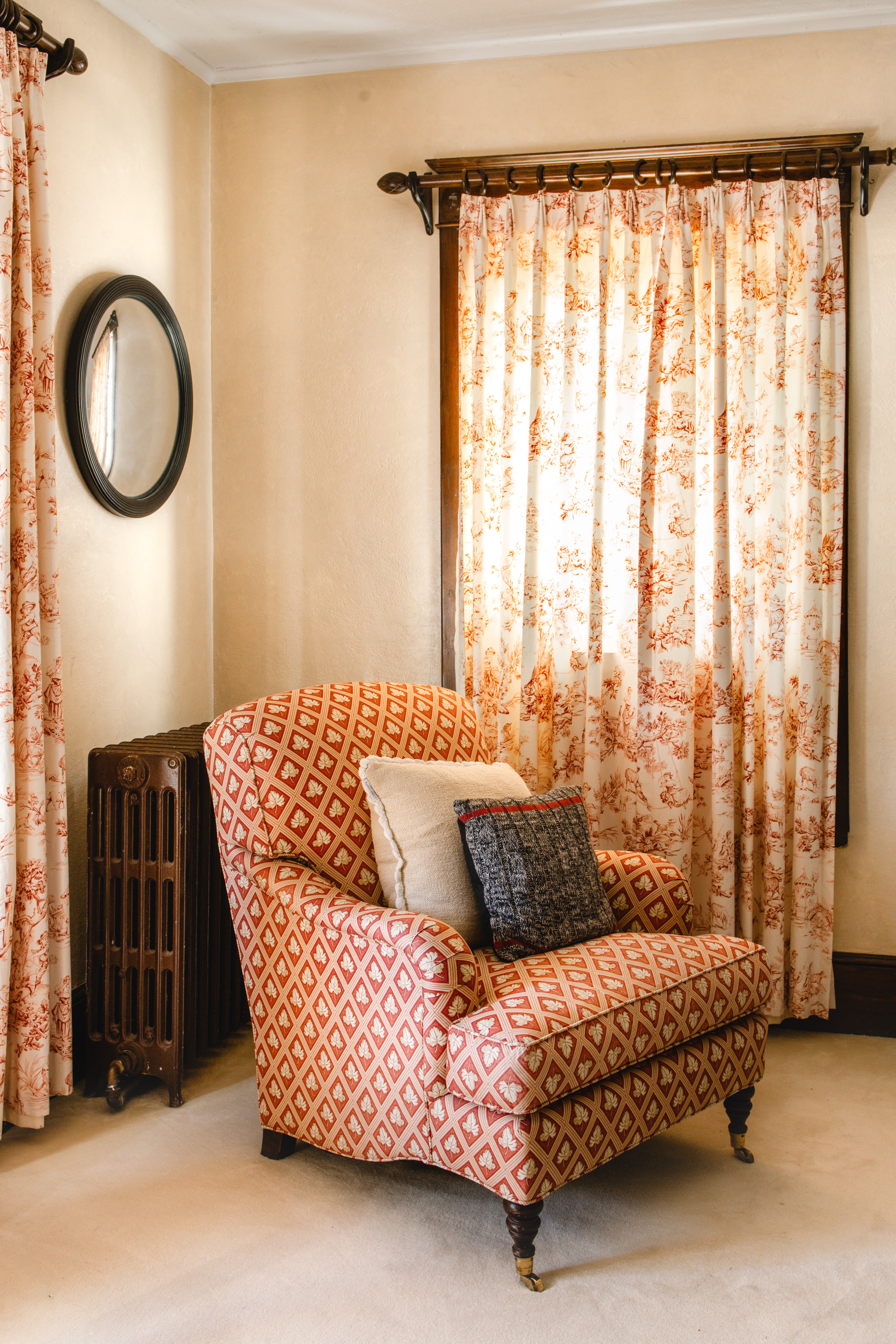 A cozy corner with a patterned armchair, decorative pillows, and floral curtains.