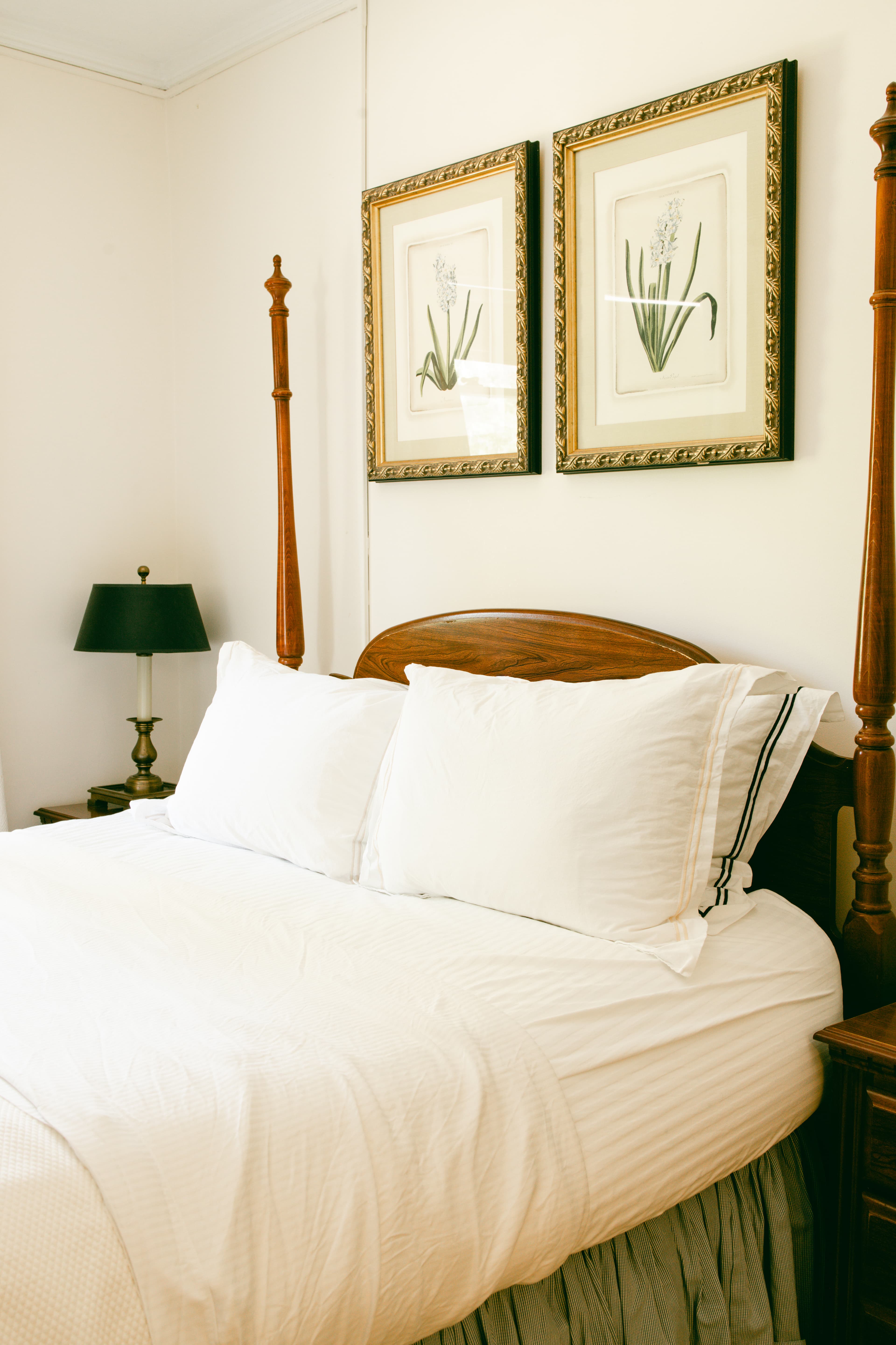 Cozy bedroom featuring a neatly made bed with white linens and framed floral artwork on the wall.