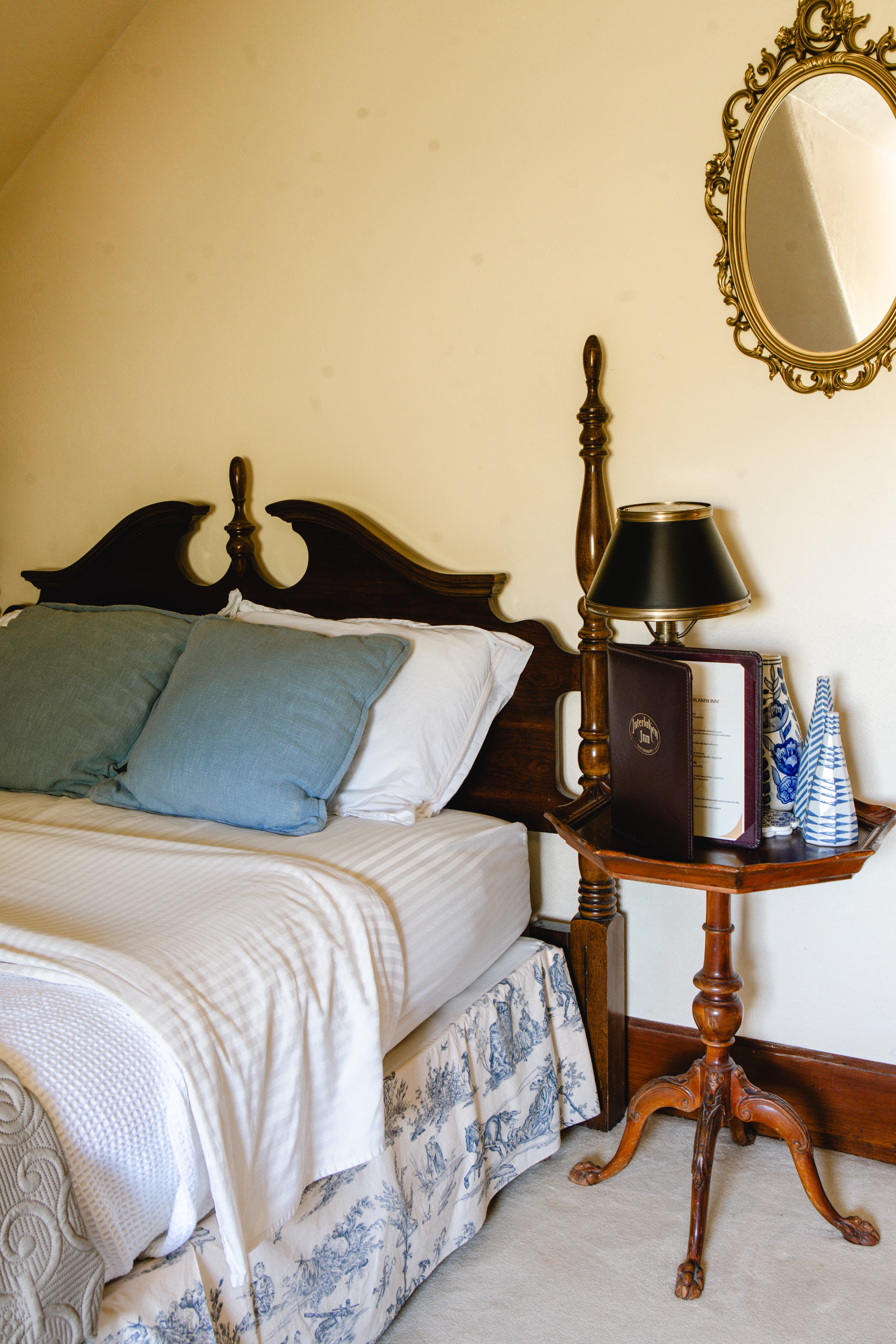 A cozy bedroom featuring a wooden bed with blue cushions, a bedside table with a lamp, and decorative accents.