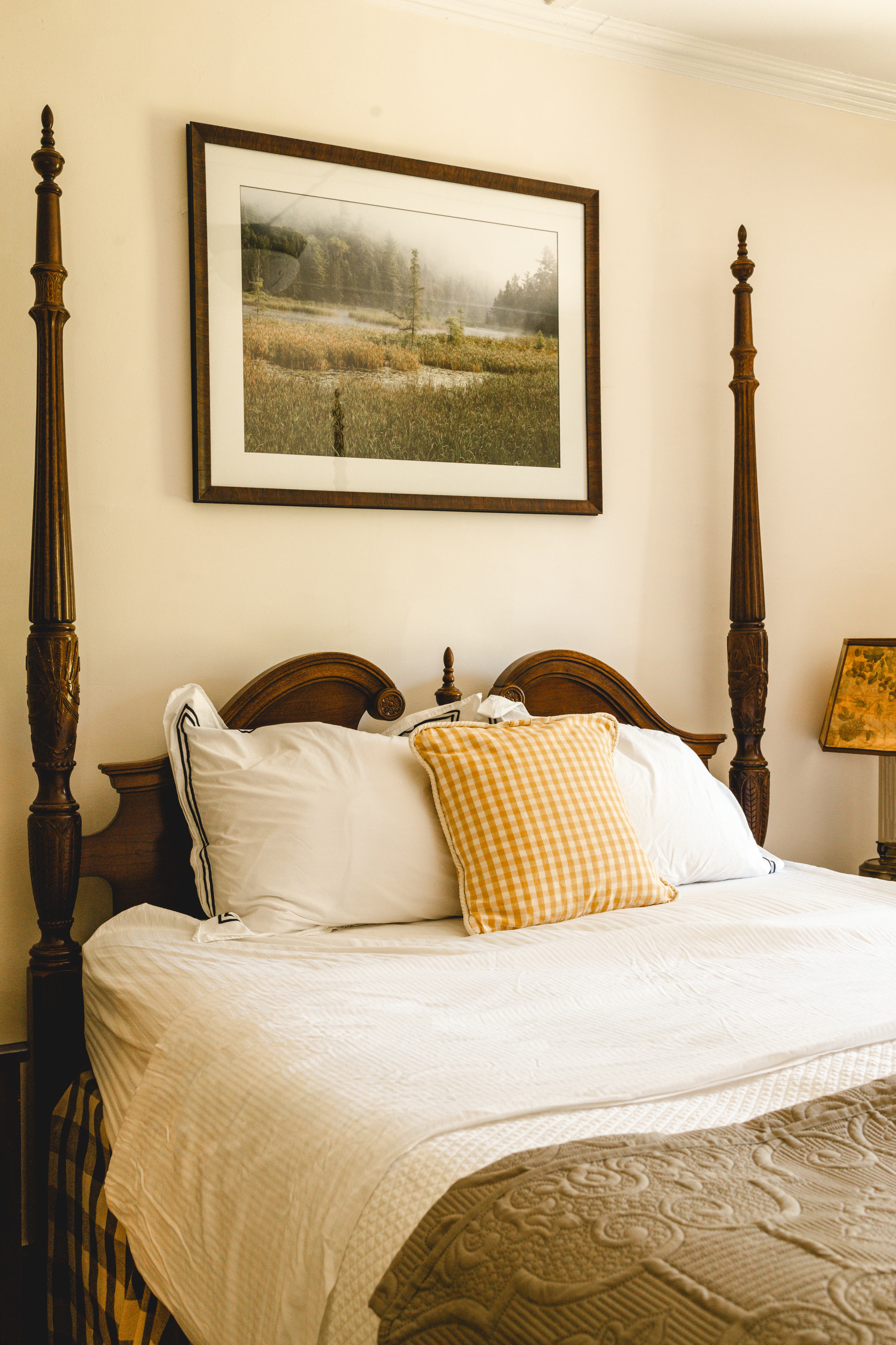 A cozy bed with a decorative pillow and a framed landscape painting above it.