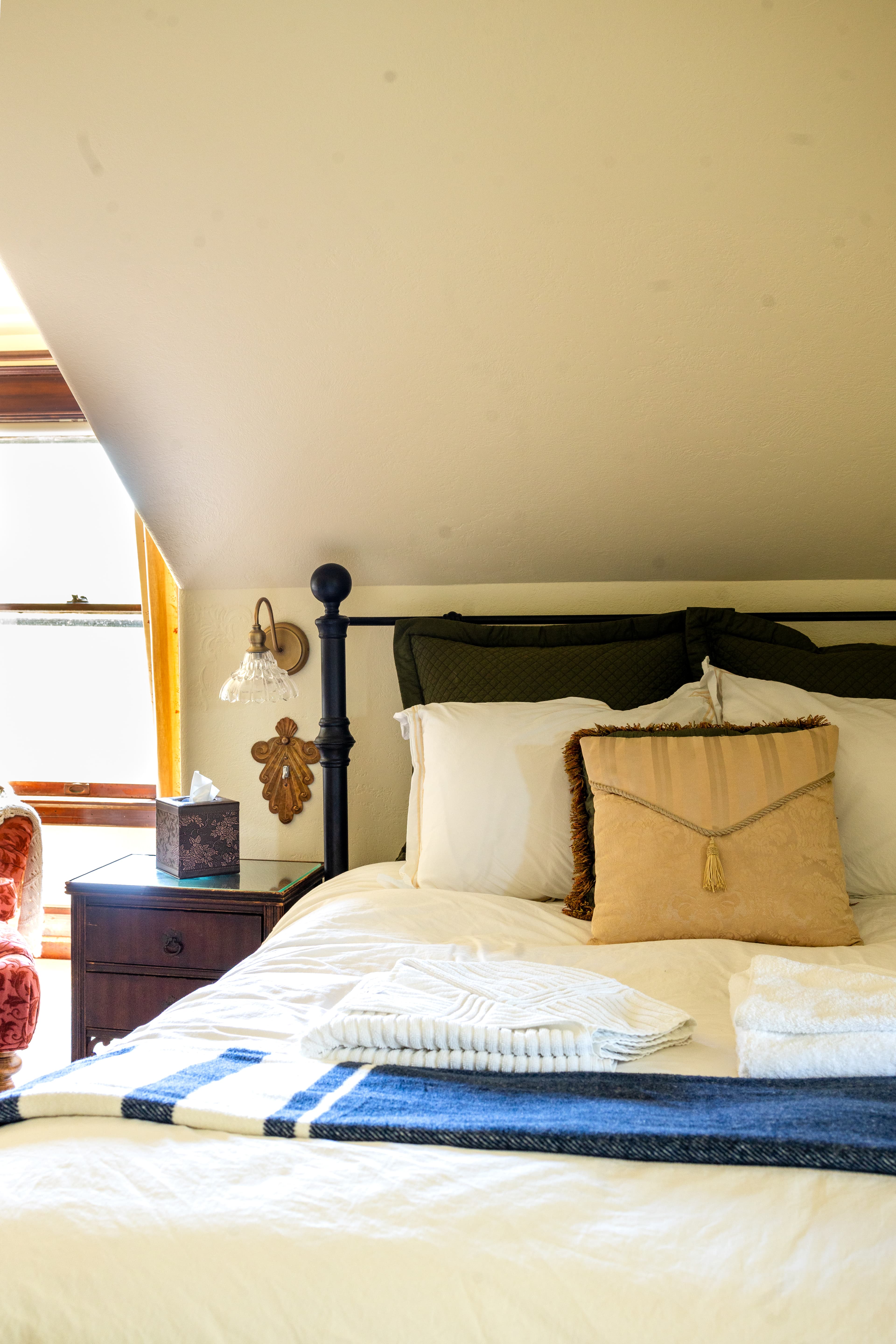 A cozy bedroom featuring a neatly made bed with decorative pillows, a blue throw blanket, and a nearby armchair.