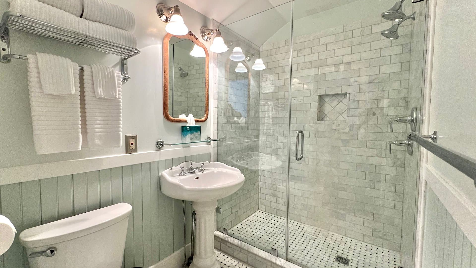 Modern bathroom with a glass shower, pedestal sink, and white towels.